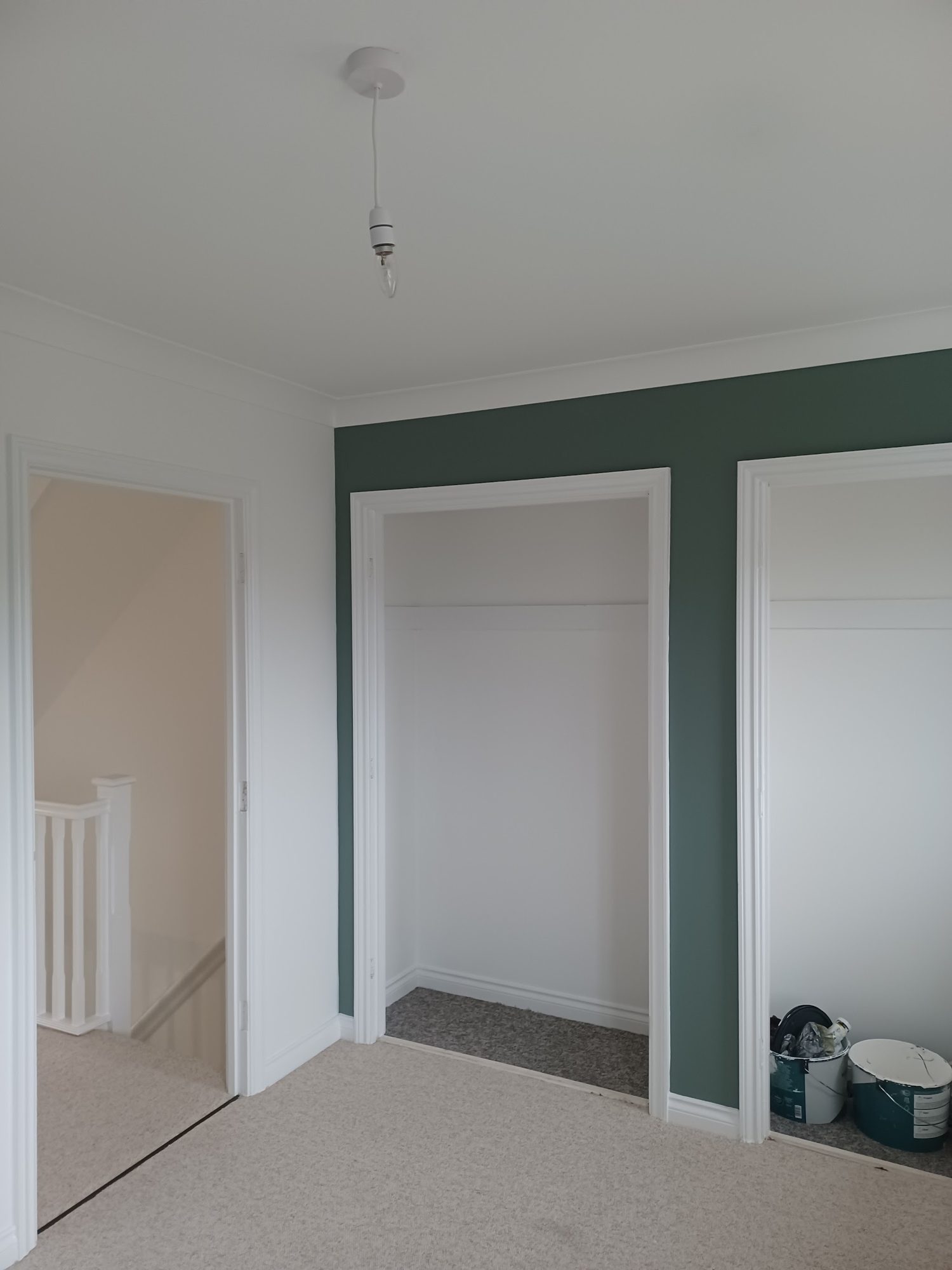 A landing with a deep green feature wall and white woodwork
