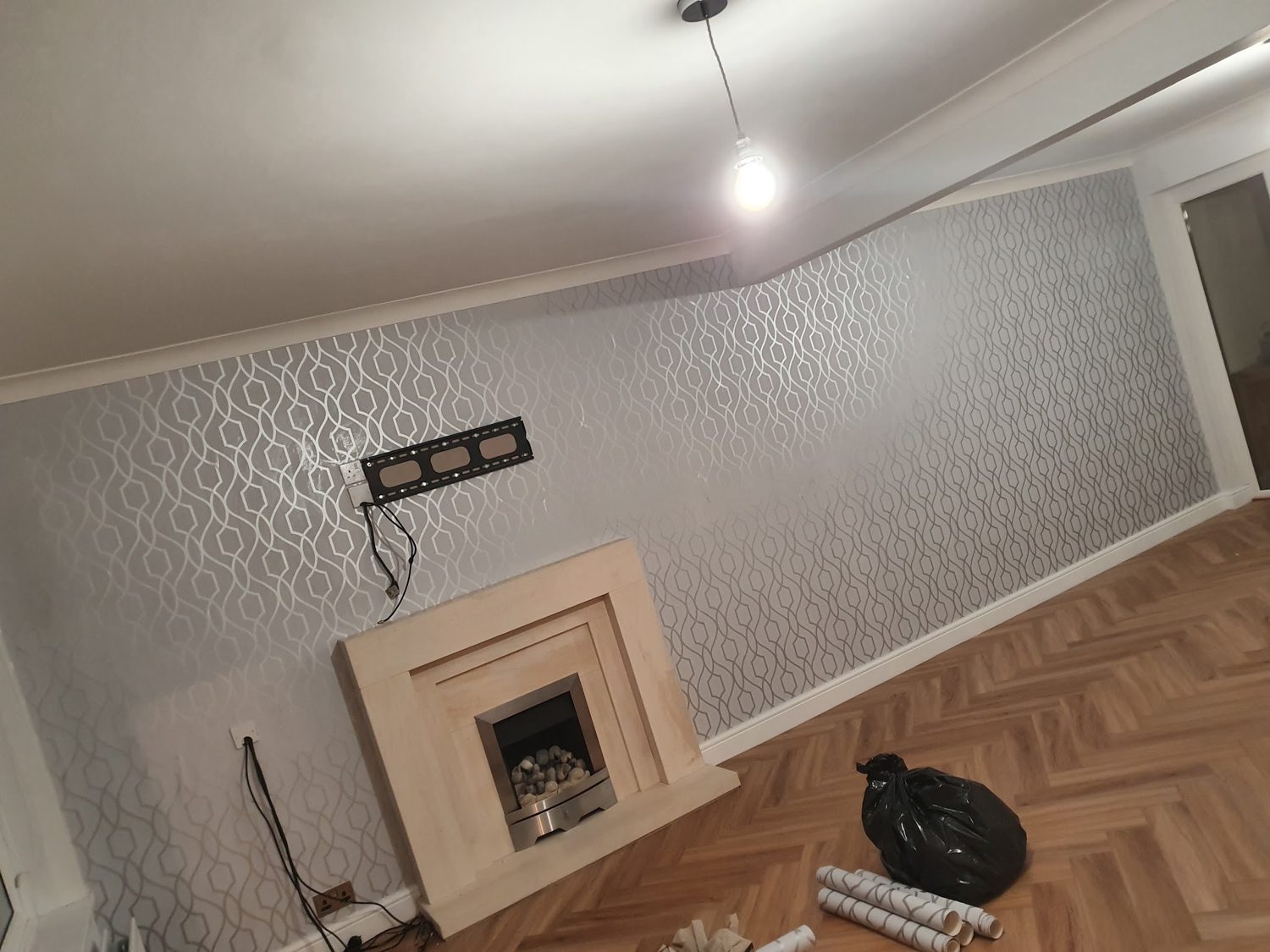 A living room with a pale geometric wallpaper behind a stone fireplace