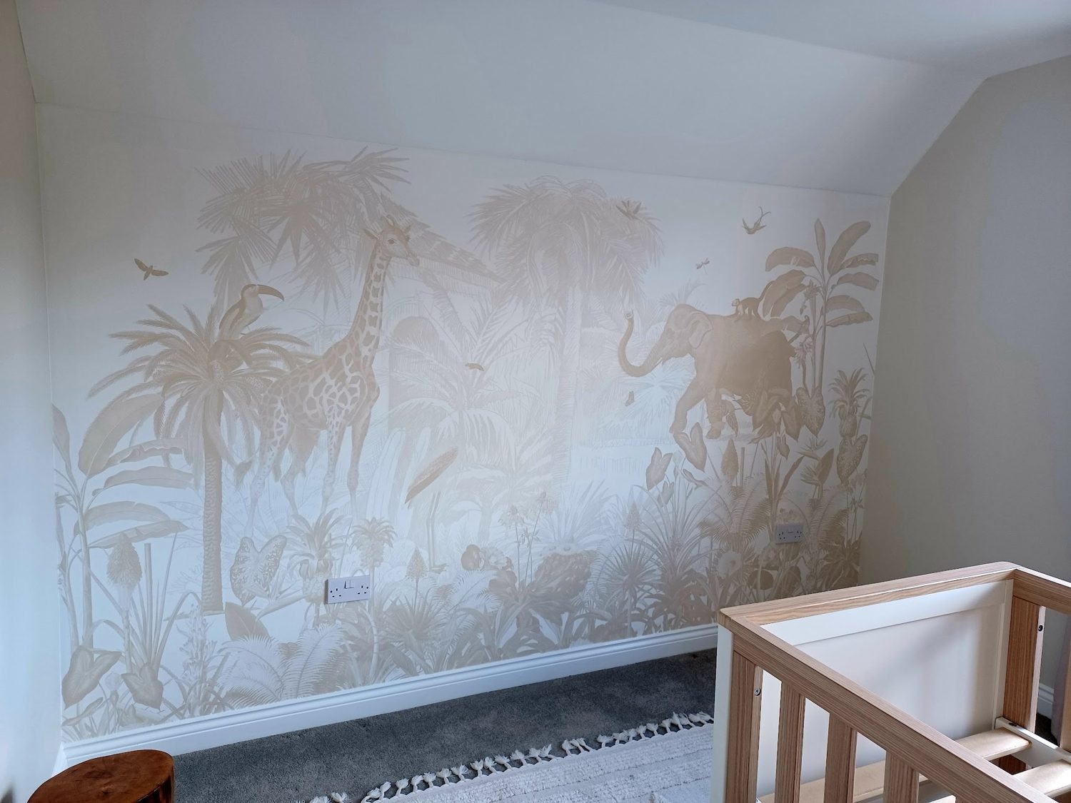 A nursery wall with a sand-coloured jungle animal mural above a cot