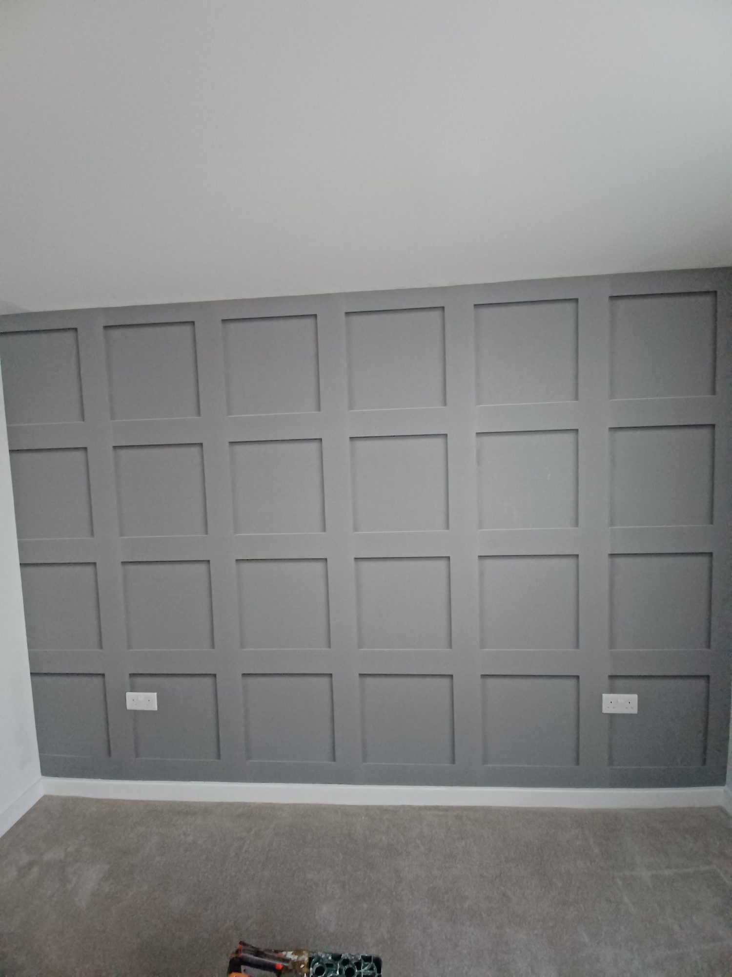A grey panelled feature wall behind a carpeted floor